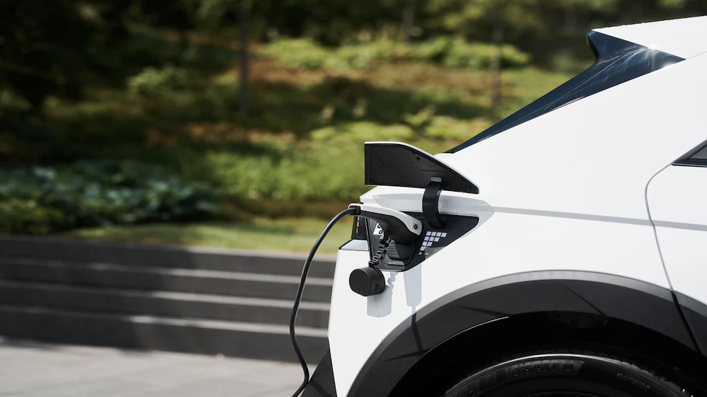 Nahaufnahme eines weissen Swisscom-Elektrofahrzeugs beim Laden an einer Ladestation im Aussenbereich.